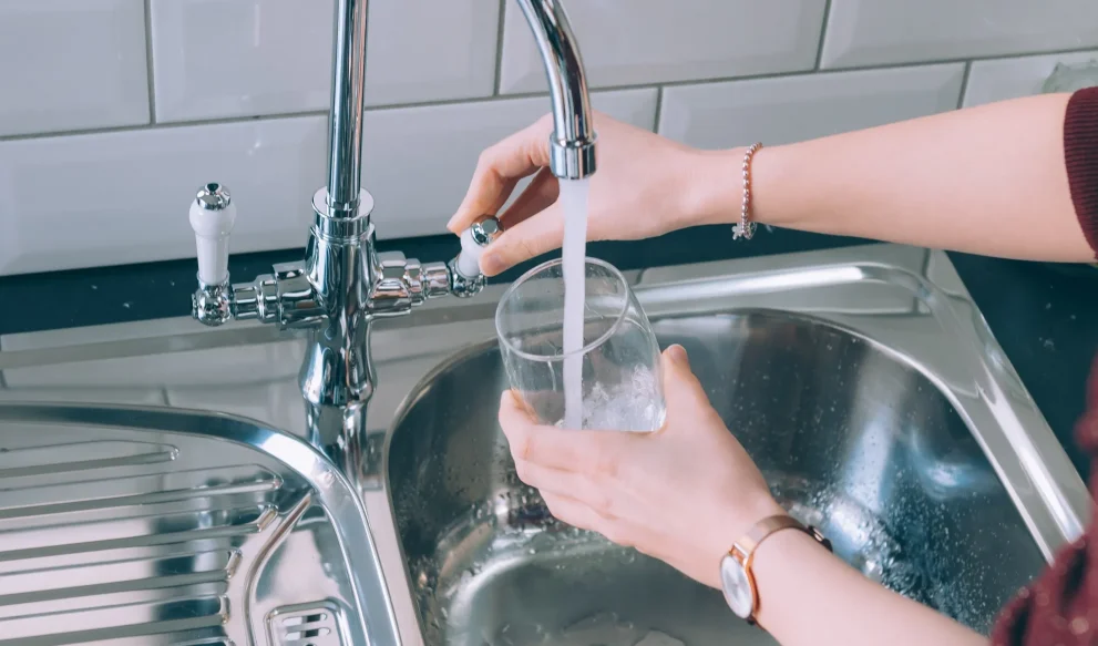 Woman Filling Glass With Water From Steel Faucet Kitchen